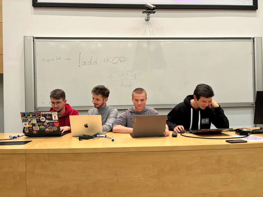 Czterech członków zarządu koła pracujących przy laptopach podczas Hackathonu organizowanego przez koło naukowe BIT.