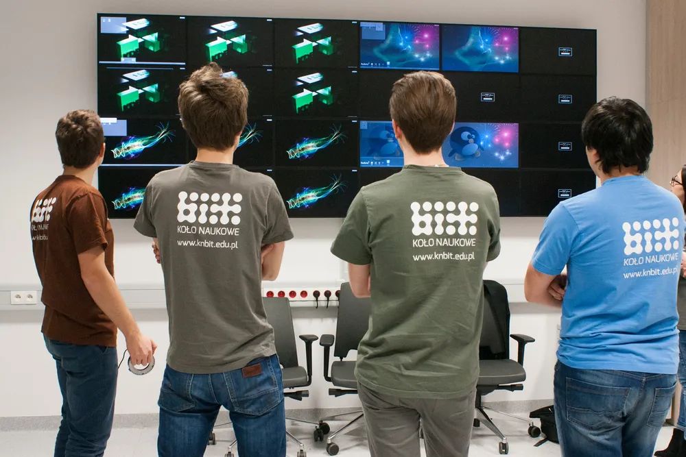 Czterech studentów w koszulkach koła naukowego BIT analizujących wyniki projektu na bardzo dużym monitorze